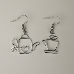 May include: A pair of silver wire earrings, one shaped like a teapot with a heart detail, and the other shaped like a coffee cup with steam rising from it.