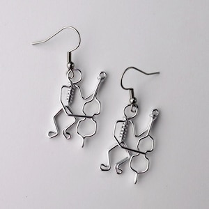 May include: A pair of silver-colored wire earrings. Each earring features a stylized musician playing a cello. The musician and cello are crafted from a single piece of wire, with a hook for the ear.