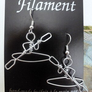 May include: Silver wire earrings shaped like a person kayaking. The earrings are on a black card with the text "Filament" and "hand-made by/fait &agrave; la main par Heather Boyd/Montreal/Canada".