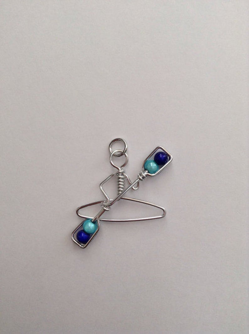 May include: A silver wire sculpture of a person in a kayak with blue and turquoise beads for paddles.