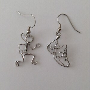 May include: A pair of silver wire earrings. One earring is shaped like a running person, the other is shaped like a running shoe.