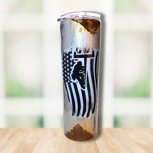 May include: A stainless steel tumbler with a distressed, rusty finish. It features a black and white graphic of an American flag with a silhouette of a lineman working on a power line.