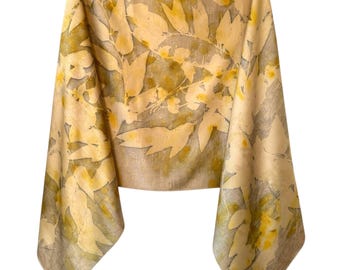 May include: A rectangular scarf featuring a botanical print with yellow and muted olive green leaf patterns on a light beige fabric background. The design displays a repeating arrangement of foliage shapes across the entire surface of the textile.