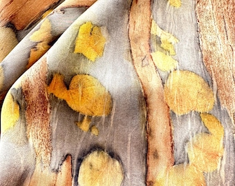 May include: A piece of fabric featuring a botanical print with a gray background. The textile displays elongated brown wood-like patterns and scattered yellow leaf-shaped imprints, creating a layered, organic visual effect across the surface.