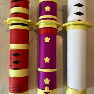 May include: Three decorative sword handles in red, purple, and white. Each handle has yellow accents and a unique design. The red handle features black crisscross details, the purple has flower accents, and the white has a wrapped design.