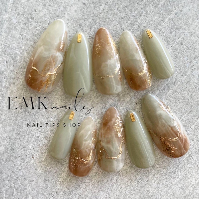 Handmade earth tone marble press-on nails in olive green, warm brown, and creamy white with delicate gold foil accents.