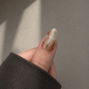 Handmade earth tone marble press-on nails in olive green, warm brown, and creamy white with delicate gold foil accents.