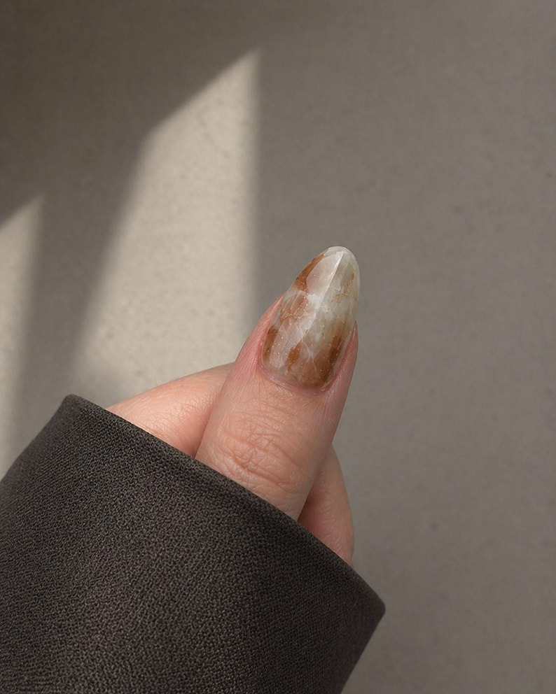 Handmade earth tone marble press-on nails in olive green, warm brown, and creamy white with delicate gold foil accents.