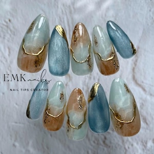 Set of ten handmade blue marble cat eye press-on nails with gold foil accents, ocean blue shimmer, and long almond shape.