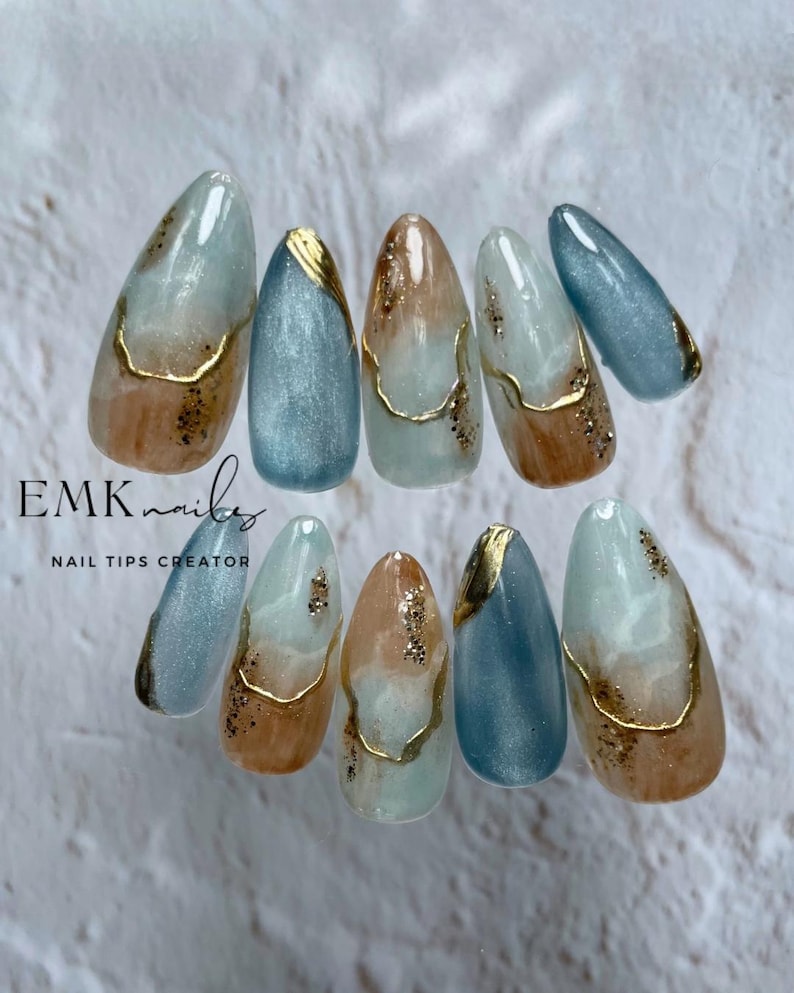 Set of ten handmade blue marble cat eye press-on nails with gold foil accents, ocean blue shimmer, and long almond shape.