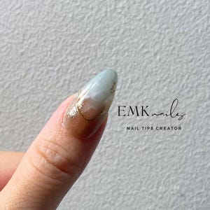 Close-up of a blue cat eye press-on nail with gold foil, marble details, and glossy gel finish.