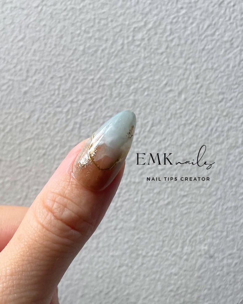 Close-up of a blue cat eye press-on nail with gold foil, marble details, and glossy gel finish.
