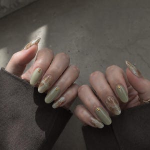 Handmade earth tone marble press-on nails in olive green, warm brown, and creamy white with delicate gold foil accents.