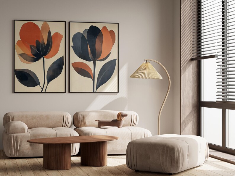 May include: Two framed abstract floral prints with orange, brown, and blue colors hang on a white wall above a beige sofa with a wooden coffee table and a beige ottoman. A floor lamp with a beige shade is in the corner.