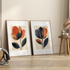 May include: Two framed prints of abstract floral illustrations. The prints are in a minimalist style with orange, brown, and black colors. The prints are framed in natural wood.