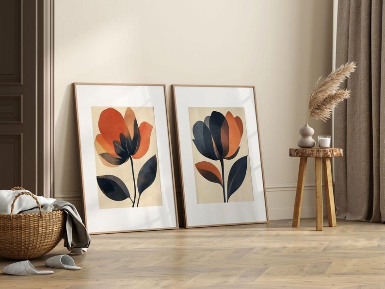 May include: Two framed prints of abstract floral illustrations. The prints are in a minimalist style with orange, brown, and black colors. The prints are framed in natural wood.