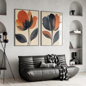 May include: Two abstract floral prints in black frames hang on a white wall above a black leather sofa with a black and white throw blanket. A black floor lamp with three round shades stands in the corner.