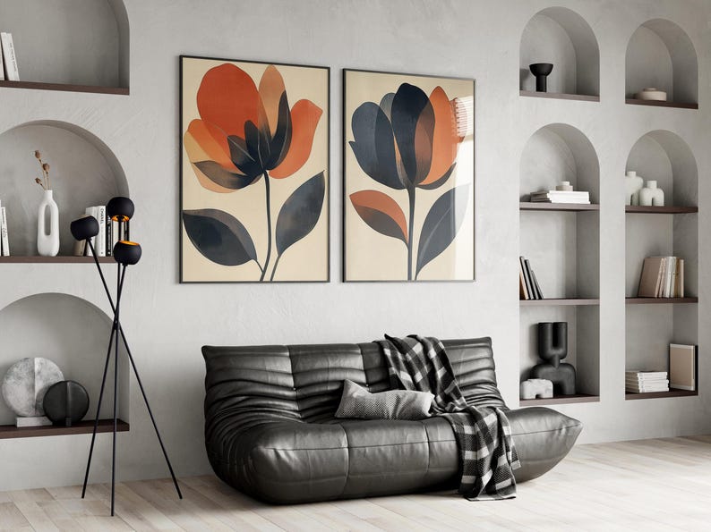 May include: Two abstract floral prints in black frames hang on a white wall above a black leather sofa with a black and white throw blanket. A black floor lamp with three round shades stands in the corner.