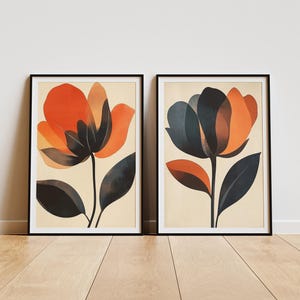 May include: Two framed prints of abstract floral illustrations. The prints feature stylized flowers with orange, red, and black petals. The background of the prints is a light beige.
