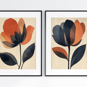 May include: Two framed abstract floral prints with a cream background. The first print features a dark blue and orange flower with dark blue leaves. The second print features a dark orange and red flower with dark blue leaves.
