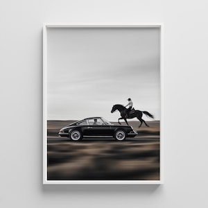 Puede incluir: Fotografía en blanco y negro de un coche deportivo negro y un jinete a caballo en una carretera desértica. La imagen sugiere velocidad y movimiento. El coche es un modelo clásico.
