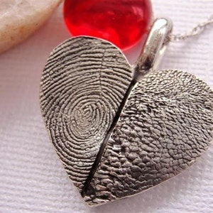 May include: A silver heart-shaped pendant necklace with two fingerprint impressions. The pendant is split in half, with each half featuring a different fingerprint.