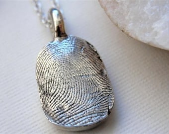 May include: A silver pendant necklace with a fingerprint design. The pendant is oval shaped and has a detailed impression of a fingerprint.
