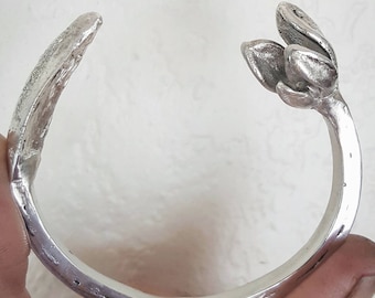 May include: A silver bracelet with a flower design. The bracelet is open and has a smooth, rounded surface.