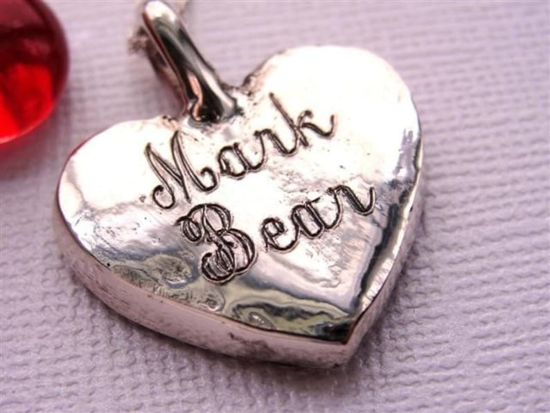 May include: Silver heart-shaped pendant with the inscription "Mark Bean" engraved on the front.