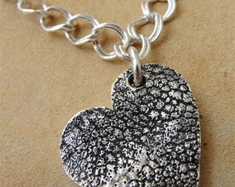 Op de afbeelding: Een zilveren ketting met een getextureerde zilveren hart hanger.