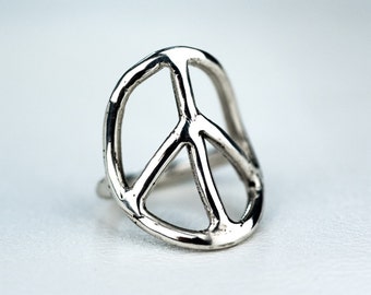 Könnte beinhalten: Ein silberner Friedenszeichenring. Der Ring ist aus Metall und hat eine glatte, polierte Oberfläche.