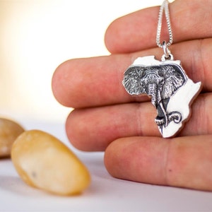 Op de afbeelding: Zilveren ketting met een hanger in de vorm van het Afrikaanse continent, met een gegraveerd olifantenhoofd in het midden.