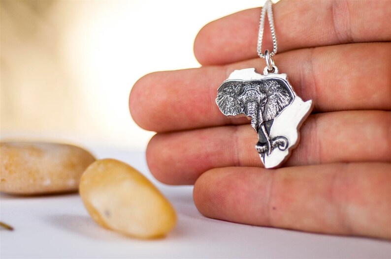 Op de afbeelding: Zilveren ketting met een hanger in de vorm van het Afrikaanse continent, met een gegraveerd olifantenhoofd in het midden.