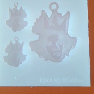 Puede incluir: Un molde de silicona transparente con tres colgantes con forma de rostro con coronas. El colgante m&aacute;s grande tiene un dise&ntilde;o detallado de rostro y corona, mientras que los m&aacute;s peque&ntilde;os tienen versiones simplificadas. El texto "Rock My World inc." es visible en la parte inferior.
