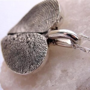 May include: A silver heart-shaped pendant necklace with a detailed textured design. The pendant is split in half and the two halves are connected by a silver chain.