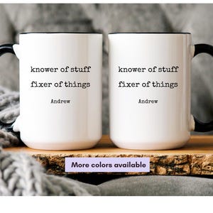 May include: Two white ceramic mugs with black handles and rims. Each mug has the text "knower of stuff, fixer of things" and the name "Andrew" printed in black. A small sign below the mugs reads "More colors available".