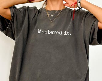 May include: A dark gray t-shirt with the phrase "Mastered it." printed in white. The shirt has a relaxed fit and short sleeves. The word "Pepper" is visible in the bottom right corner.