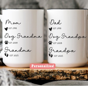 May include: Two white ceramic mugs with black handles and rims. One mug says "Mom" and "Dog Grandma" with the text "EST 1998" and "EST 2008". The other mug says "Dad" and "Dog Grandpa" with the text "EST 1998" and "EST 2008". The word "Personalized" is on a pink rectangle.