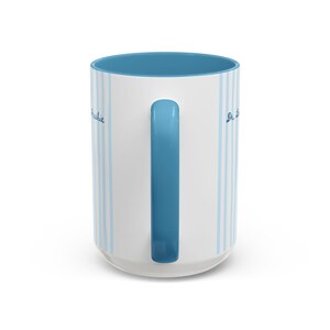 May include: A white ceramic mug featuring vertical light blue stripes and a solid blue handle. The interior of the mug is also blue. The text "Archie" is printed in blue script on the left side, and "Dr. L" is printed in blue script on the right side.