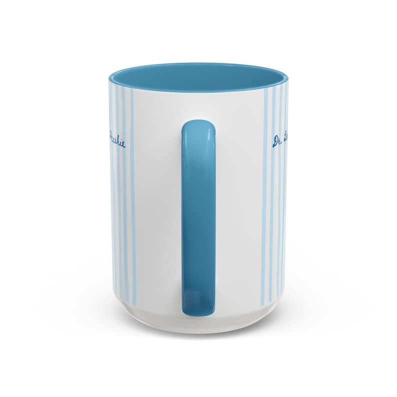 May include: A white ceramic mug featuring vertical light blue stripes and a solid blue handle. The interior of the mug is also blue. The text "Archie" is printed in blue script on the left side, and "Dr. L" is printed in blue script on the right side.