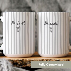 May include: Two white ceramic mugs featuring a vertical gray striped pattern. Each mug displays the text Dr. Scott in a dark gray script font, positioned above a small, simple line-drawn bow icon. The mugs have solid black handles and rims.