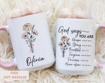May include: Two white ceramic mugs with light pink handles and interiors. One mug features a floral bouquet illustration and the name Olivia. The other mug displays a floral bouquet and the text God says YOU ARE Unique, Strong, Beautiful, Forgiven, Precious, Never alone with Bible verse references.