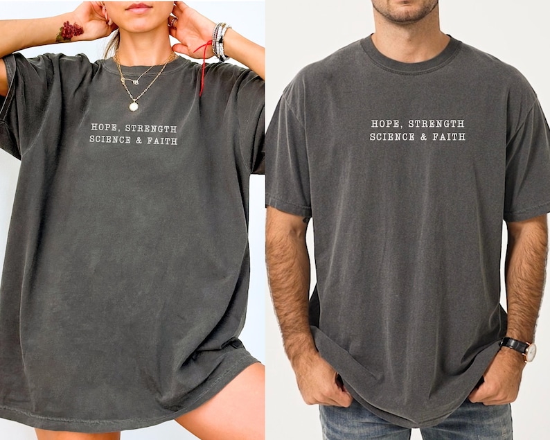 May include: A charcoal grey short-sleeve t-shirt featuring the white text HOPE, STRENGTH SCIENCE & FAITH printed on the chest. The garment has a crew neckline and a relaxed fit, showcasing a washed-out, vintage-inspired fabric texture.