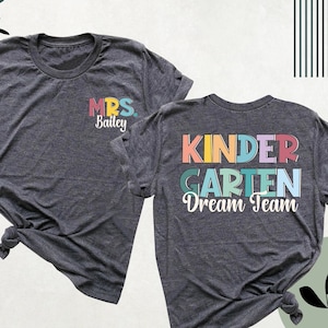 May include: Two gray t-shirts with a rainbow colored graphic on the back of one shirt that says "Kindergarten Dream Team". The other shirt has a small graphic on the front that says "Mrs. Bailey".