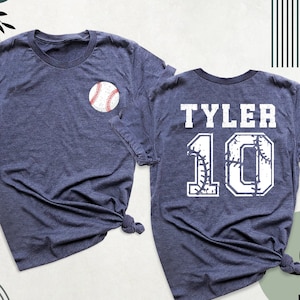 May include: A navy blue t-shirt with a white baseball graphic on the front and the text "TYLER 10" with a baseball graphic on the back.