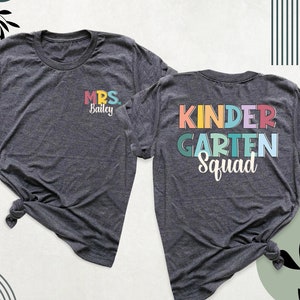 May include: Two grey t-shirts with a rainbow colored design. The front of one shirt says "MRS. Bailey" and the back of the other shirt says "KINDERGARTEN SQUAD".