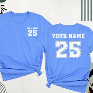 May include: Two light blue t-shirts with a white number 25 printed on the front and back. The front shirt says "Team Name" above the number. The back shirt says "Your Name" above the number.