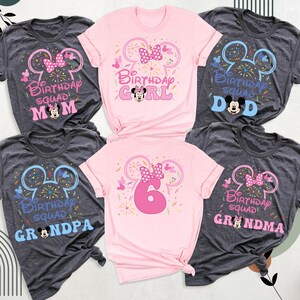 May include: A collection of gray and pink t-shirts with birthday-themed designs. Each shirt features a Minnie Mouse ear silhouette, a bow, and the words "Birthday Squad" along with roles like "Mom," "Girl," "Dad," "Grandpa," and "Grandma."