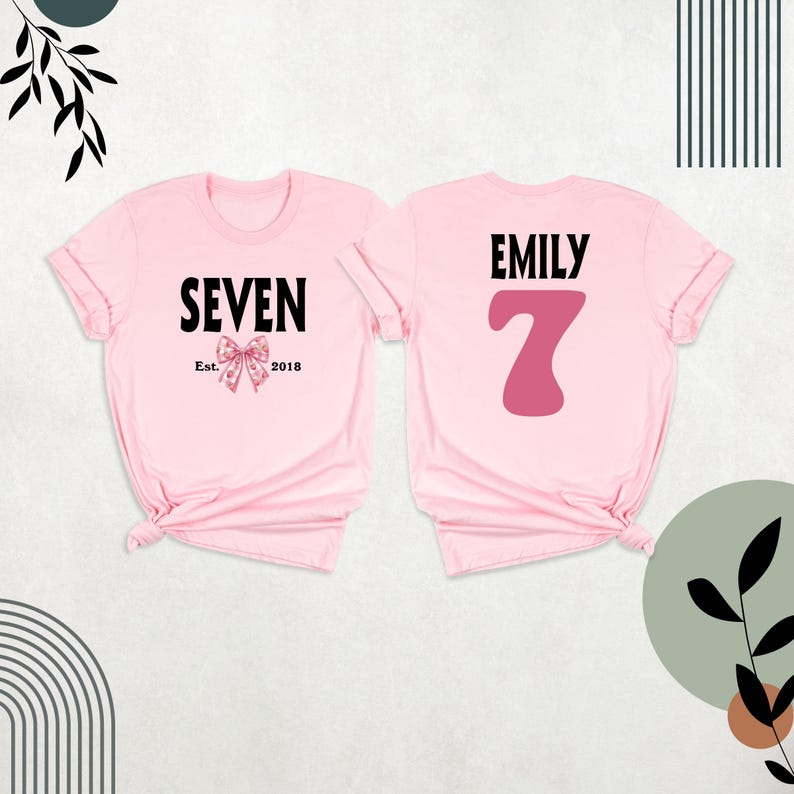Peut inclure: Deux t-shirts roses, l'un avec le texte "SEVEN Est. 2018" et un n&oelig;ud rose, l'autre avec le texte "EMILY" et un grand chiffre 7 rose.