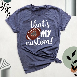 K&ouml;nnte beinhalten: Ein marineblaues T-Shirt mit dem Text "that's my custom!" und einem braunen Fu&szlig;ball mit der Nummer 8 darauf.
